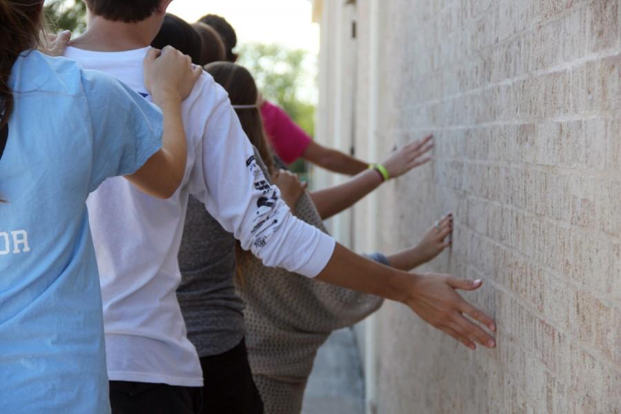 A group blind-folded Teen Teachers uses the wall as a point of contact during the trust exercize.